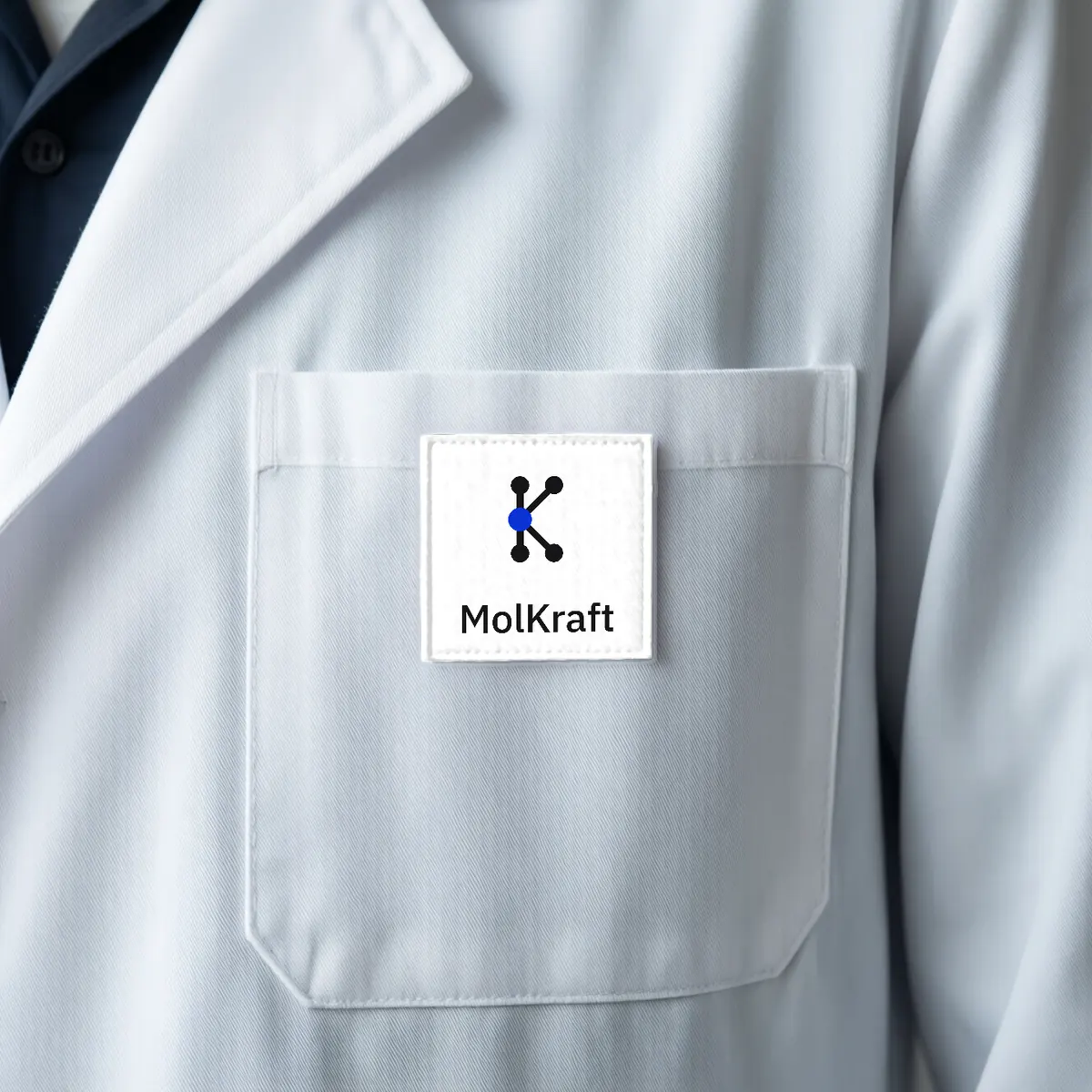 A white lab coat pocket with an embroidered MolKraft logo patch.